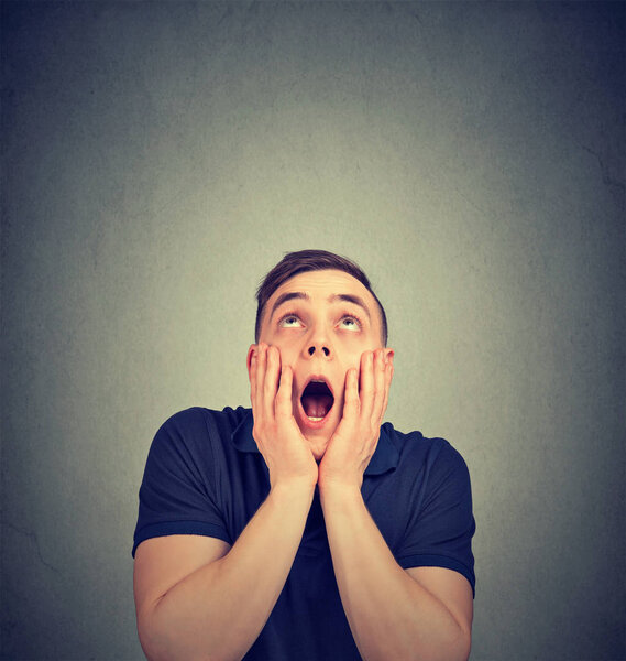 Случайный молодой человек, держась за щеки и глядя вверх в выражении страха и изумления
