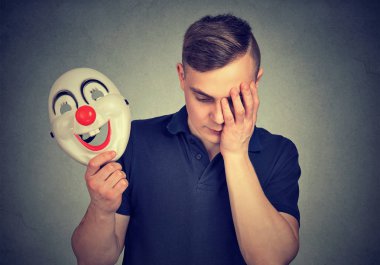 Renkli palyaço maskesi tutarak ve üzgün olmak depresyon ve duyguları gizleme arıyor genç adam 