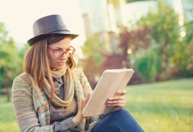 Şık Bayan şapka ve gözlük yeşil park tek başına oturmak dinlenirken tablet sörf soğutma 