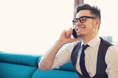 Telefon görüşmesi olması ve evde kanepede otururken gülümseyen bardakları neşeli şık adam