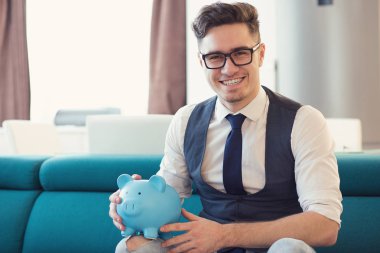 Mavi kumbara Divan kameraya gülümseyen yeni modern apartmanda oturan tutan bardaklarda mutlu resmi adam