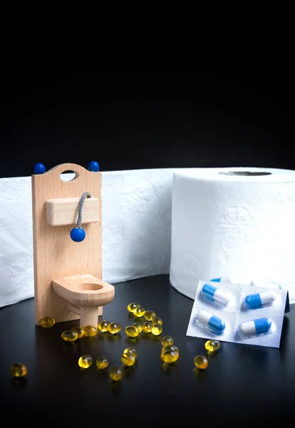 Wooden toy toilet, capsules and paper on black background