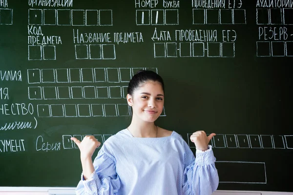 ロシアの学校で試験の記入サンプルと黒板に対して親指を示す女子高生 — ストック写真
