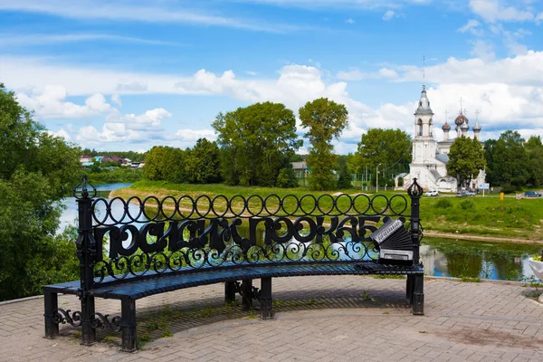 Oggetto d'arte panca in ghisa con fisarmonica e parole "Sediamoci e acqua" su argine di fiume e Chiesa della Presentazione — Foto Stock