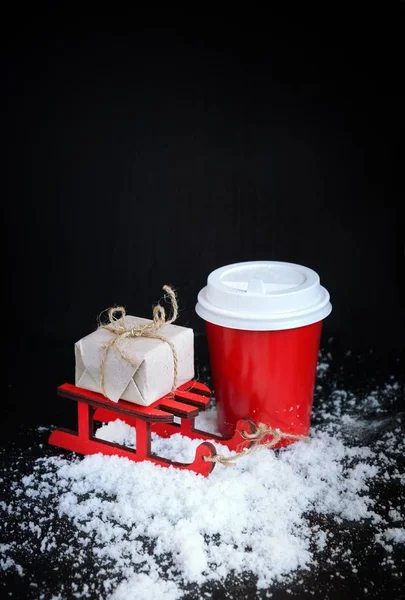 Café para ir em copo vermelho, trenó e natal presente no fundo preto. Bebidas quentes no inverno frio — Fotografia de Stock