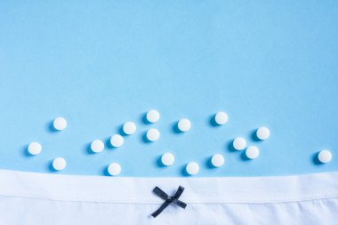 Yaylı beyaz kadın külodu ve mavi arka planda haplar. Jinekoloji ve üroloji. Sağlık, doğum kontrol, planlı hamilelik, sistit. Boşluğu kopyala