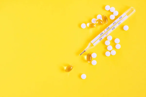 Glass mercury thermometer, white pills and capsules on yellowbackground. Fever heat, antipyretic tablets, cold. — Stock Photo, Image
