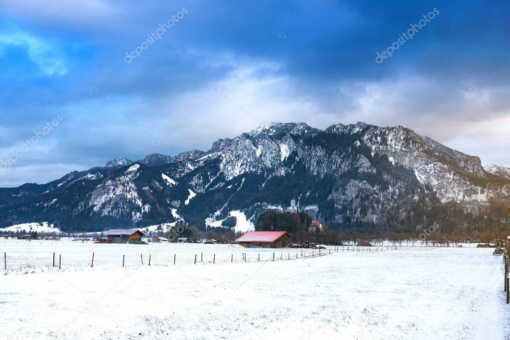 Wooden shed in snowy field against Alps in winter day. Schwangau, Bavaria, Germany