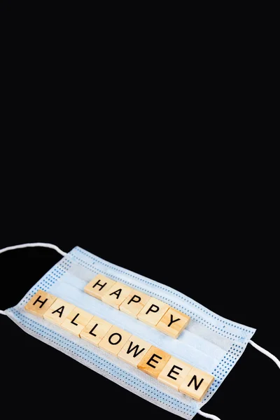 Medical mask and wooden words Happy Halloween on black. Halloween background decor holiday concept. Vertical. Copy space