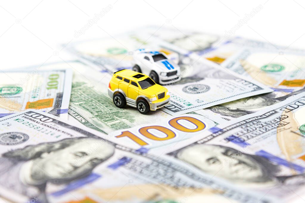 Two small toy cars on dollars. Car purchase and insurance. Car rental, repair, maintenance. Business in automobile industry