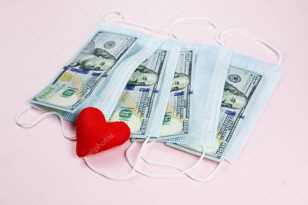 Red heart,medical masks and dollars on pink.Helping poor countries with money and masks.Financial crisis due to coronavirus.Cash payments to doctors.Expensive hospital services. Medical research.