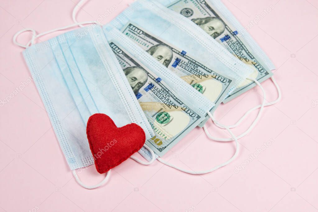 Red heart,medical masks and dollars on pink.Helping poor countries with money and masks.Financial crisis due to coronavirus.Cash payments to doctors.Expensive hospital services. Medical research.