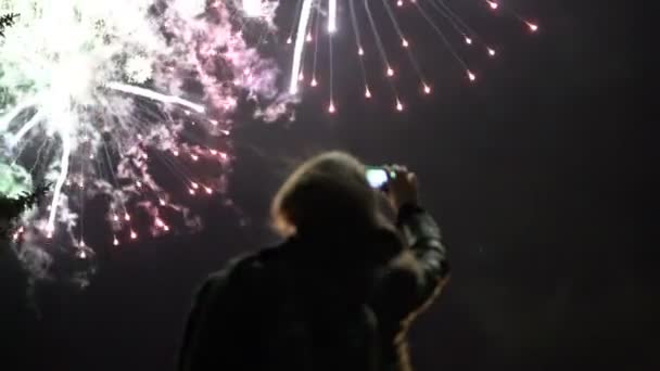 少女は、携帯電話で花火の写真を撮る。ライトに照らされた空の背景のシルエット. — ストック動画