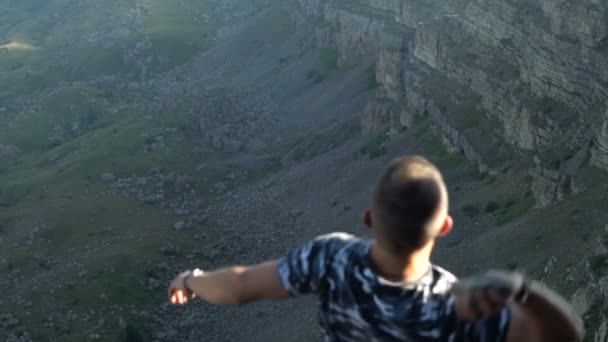 Een jonge man staat op de rand van een klif en gooit een steen naar beneden in de afgrond Stockvideo