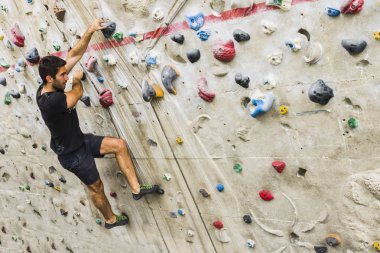 İçerideki yapay duvarda kaya tırmanışı pratiği yapan bir adam. Etkin yaşam tarzı ve kayalık kavramı.