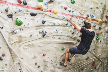 İçerideki yapay duvarda kaya tırmanışı pratiği yapan bir adam. Etkin yaşam tarzı ve kayalık kavramı.