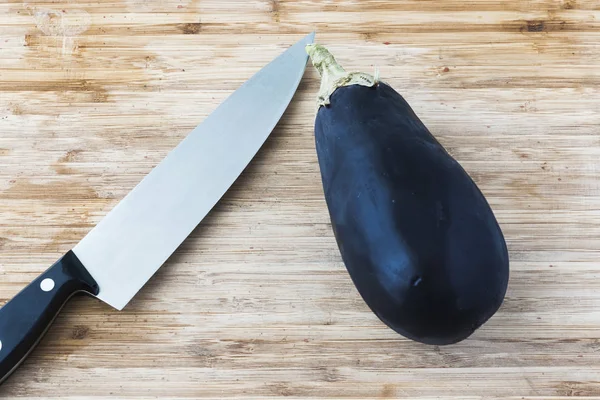 One Aubergine on wooden board with a knife and copy space