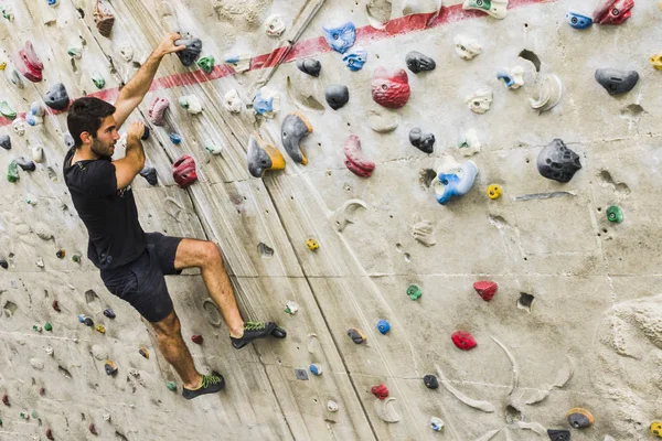 İçerideki yapay duvarda kaya tırmanışı pratiği yapan bir adam. Etkin yaşam tarzı ve kayalık kavramı.