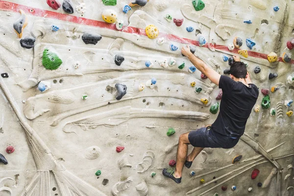 İçerideki yapay duvarda kaya tırmanışı pratiği yapan bir adam. Etkin yaşam tarzı ve kayalık kavramı.