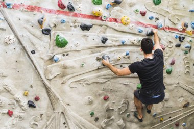 İçerideki yapay duvarda kaya tırmanışı pratiği yapan bir adam. Etkin yaşam tarzı ve kayalık kavramı.