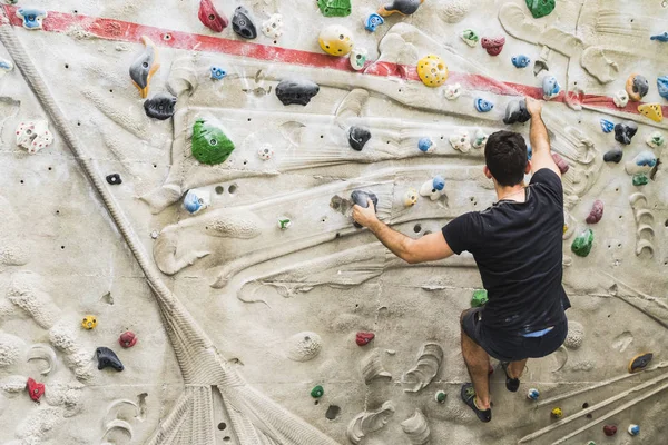 İçerideki yapay duvarda kaya tırmanışı pratiği yapan bir adam. Etkin yaşam tarzı ve kayalık kavramı.