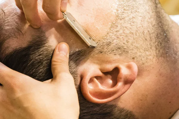 Two hands shaving a man\'s beard