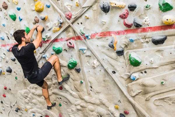 Hombre practicando escalada en roca en paredes artificiales en interiores. Activo — Foto de Stock