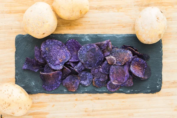 Heap de batatas fritas roxas no fundo de madeira — Fotografia de Stock