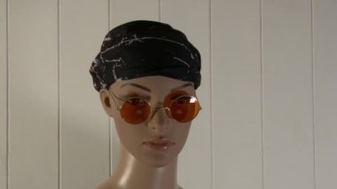 Kadın manken, güneş gözlüğü ve renkli bant 4K 59.94 fps ile moda videosu için yakın plan poz veriyor.