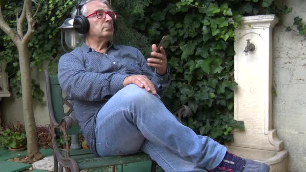 スマートフォンに接続されているヘッドフォンで何かを聞いている間にポーズをとっているイタリアのヨーロッパ人のクローズアップ — ストック動画