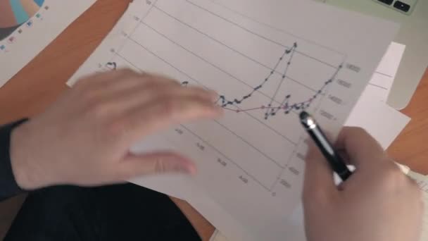 Blick von oben auf die Hand eines jungen erfolgreichen Mannes, der an der Wirtschaftsstatistik schreibt — Stockvideo