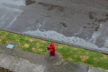 Issız bir mahallede yağmurlu bir günde uzun süre yağmura maruz kalan kırmızı bir yangın musluğu..