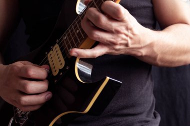 Siyah tişört giyen, siyah ve sarı elektro gitar çalan, tahta arka planda yaşayan bir adama yakın çekim. Rock & roll ve müzik konsepti
