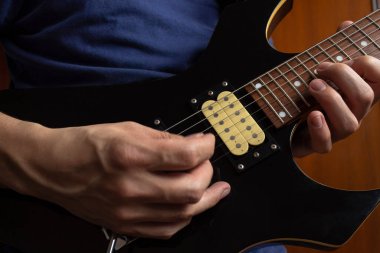 Mavi bir donanma tişörtü giyen, tahta arka planda siyah ve sarı elektro gitar çalan bir adama yakın çekim. Rock & roll ve müzik konsepti