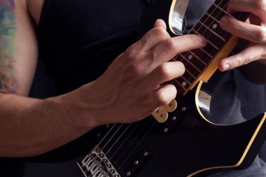 Siyah tişört giyen, siyah ve sarı elektro gitar çalan, tahta arka planda yaşayan bir adama yakın çekim. Rock & roll ve müzik konsepti