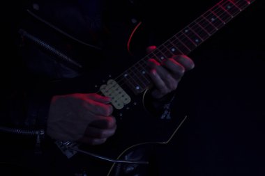 Kapalı alanda kırmızı ve beyaz ışıklarla aydınlatılmış siyah ve sarı elektro gitar çalan deri ceketli bir adamın uzun pozlama fotoğrafı. Rock ve müzik konsepti