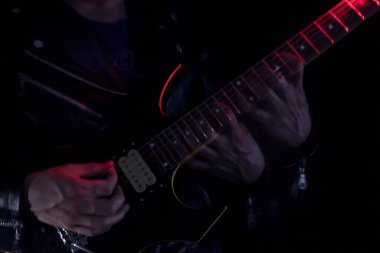  Kapalı alanda kırmızı ve beyaz ışıklarla aydınlatılmış siyah ve sarı elektro gitar çalan deri ceketli bir adamın uzun pozlama fotoğrafı. Rock ve müzik konsepti