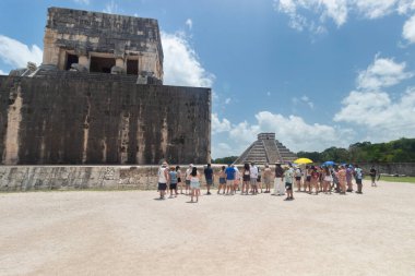 Jaguar tapınağı ve top sahasının yakınındaki antik Maya harabelerine yakın bir grup turist. Arka planda kukulkan tapınağı olan Chichen Itza arkeoloji sahasına.
