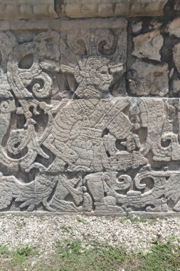 Oyun sahasındaki savaşçı bir top karakterinin Chichen Itza arkeolojik alanına oyulmuş taş bir duvara yakın dur.
