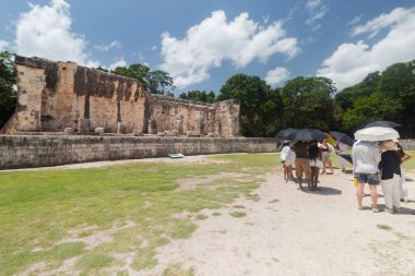 Şemsiyeli bir grup ziyaretçi, Chichen Itza arkeolojik alanına eski bir Maya oyun sahası harabelerinin yakınına geldi.