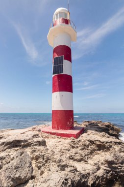 Arka planında Atlantik Okyanusu olan kayalık bir sahilin tepesindeki antika kırmızı ve beyaz bir fenere yakın.