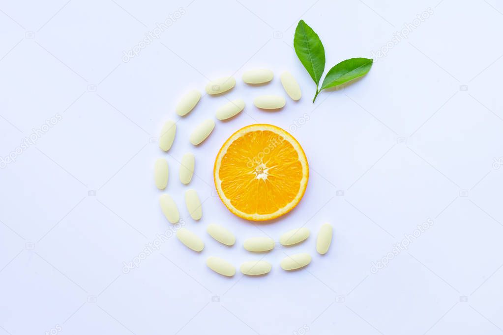 Vitamin C  pills with orange fruit on white background.