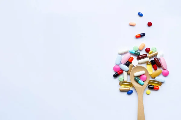 Comprimidos coloridos, cápsulas y pastillas con cuchara de madera sobre blanco — Foto de Stock