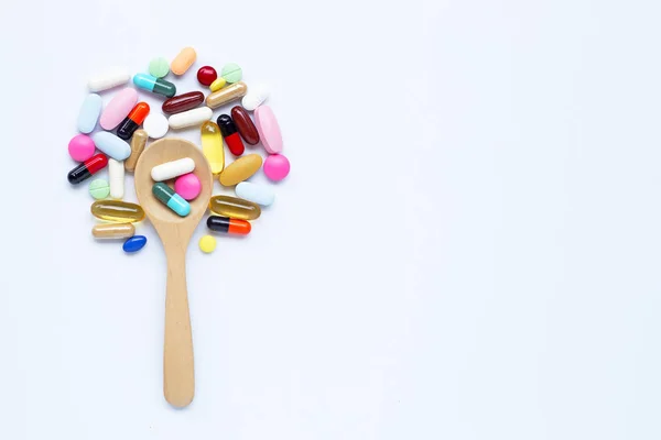 Comprimidos coloridos, cápsulas y pastillas con cuchara de madera sobre blanco — Foto de Stock