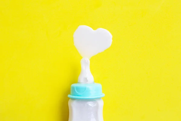 Бутылка молока для малыша на желтом фоне. Форма молочного сердца — стоковое фото