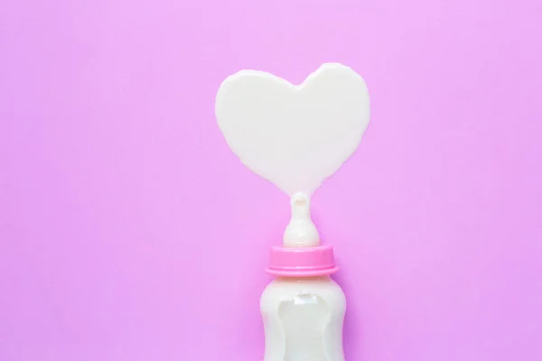 Бутылка молока для малыша на розовом фоне. Форма молочного сердца — стоковое фото