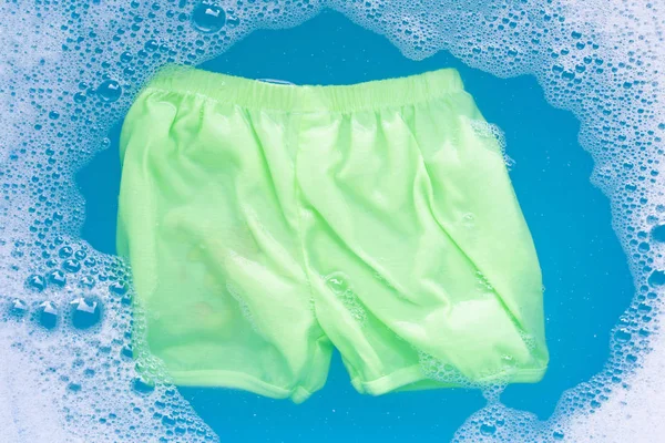 Pantalones cortos verdes del bebé empapan en agua del detergente de la ropa del bebé dissoluti — Foto de Stock