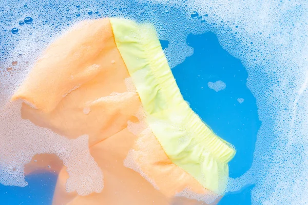 Yellow and orange baby shorts soak in baby laundry detergent wat