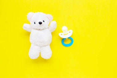 Sarı arka plan üzerinde oyuncak beyaz ayı ile bebek emzik. 