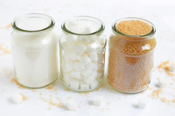 Різні види цукру в скляній банці на білому — стокове фото